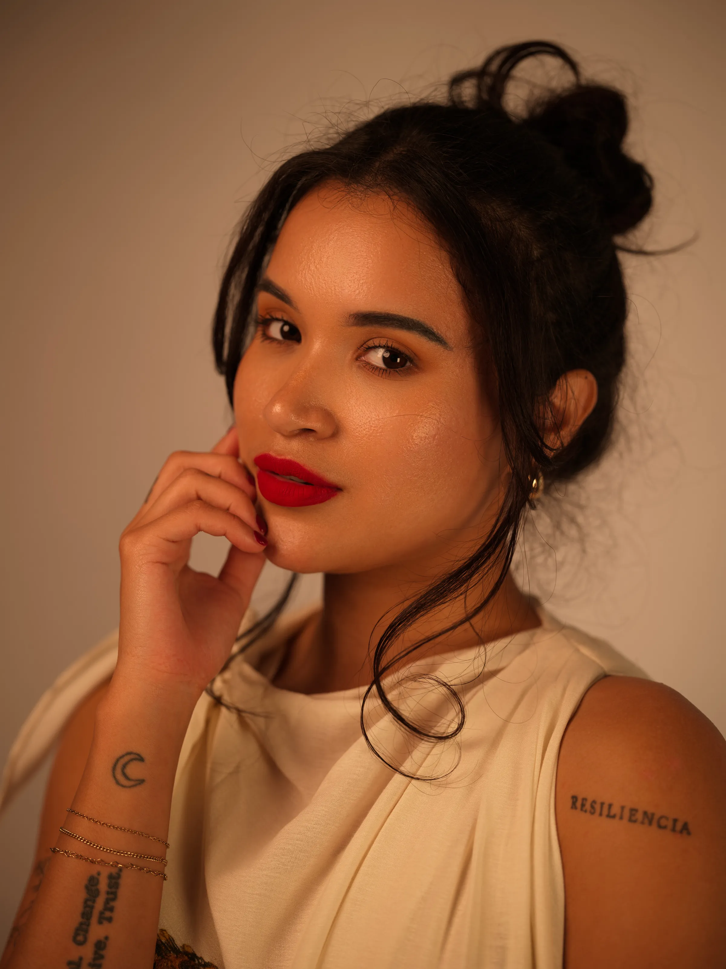 Woman with a hair bun and bold red lipstick on a warm beige backdrop.
